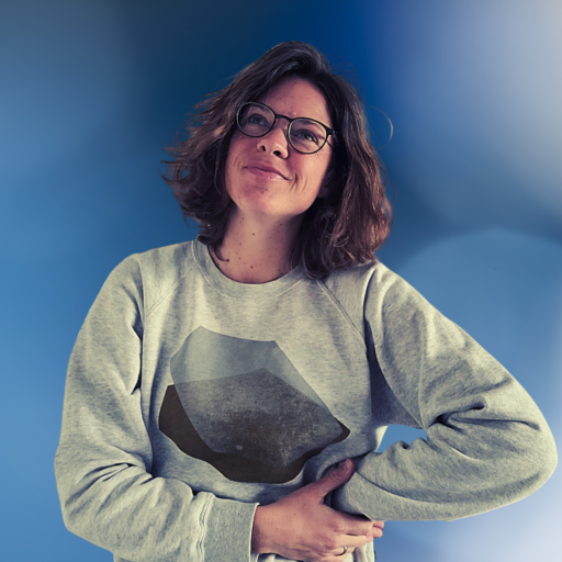 Porträtfoto von Charlotte Echterhoff, Moderatorin und Trainerin für digitale Bildung. Sie steht vor einem blau-weißen Gradient-Hintergrund, trägt eine Brille und einen grauen Pullover mit geometrischem Muster. Ihre Arme sind leicht verschränkt, und sie lächelt selbstbewusst in die Kamera – eine einladende und professionelle Ausstrahlung.
